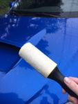 An adhesive lint roller is held in front of a blue car 