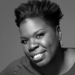 Photo shows Leslie Jones headshot from SNL. She's smiling at the camera with her short hair upswept and she is wearing small hopp earings and a scoopneck shirt.